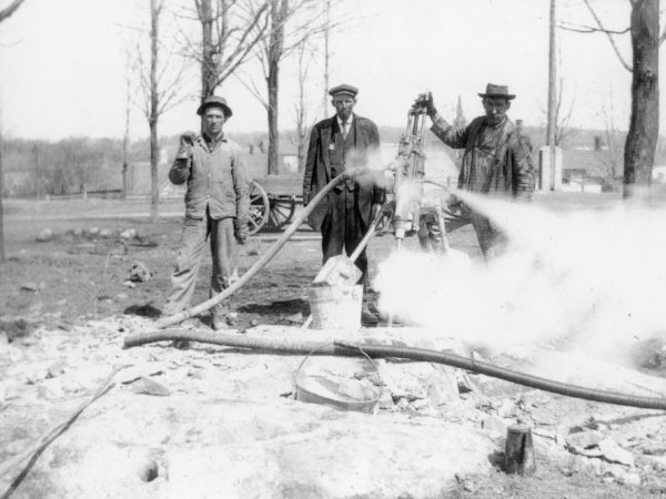 Three workers from the town road crew using a steam drill on school hill. 1910. De Kalb Junction, NY. Photograph by Robert Woodward.