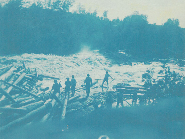 Loggers stand on the banks of the Racquette River during a log drive in Colton