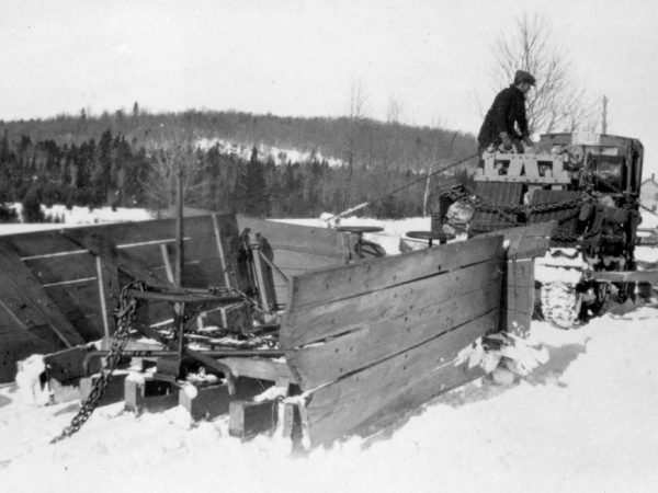 Man atop a wooden snow plow in Long Lake