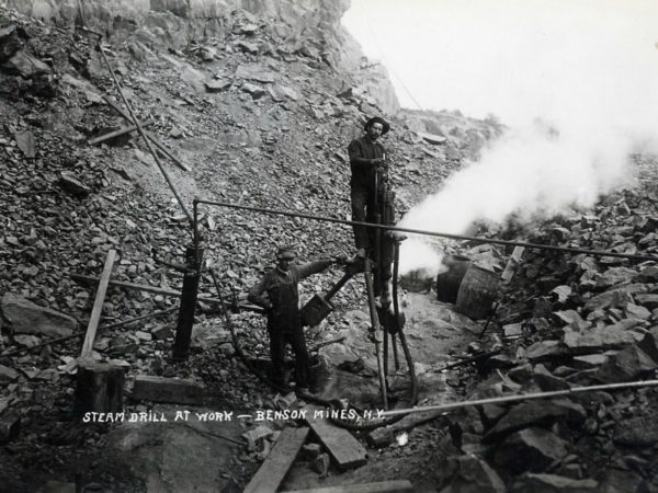 Two miners with a steam drill in the pit at Benson Mines