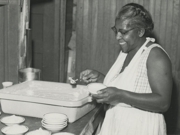 Preparing for a meal in the kitchen of the Echo Camp for Girls. Unidentified African-American cook. Photograph by Edward P. Fynmore of Fynmore Studios. 1950-1970. Raquette Lake, NY. Courtesy of the Adirondack Experience