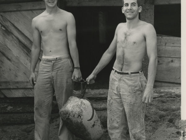 Two men hold a block of ice with tongs in Boonville