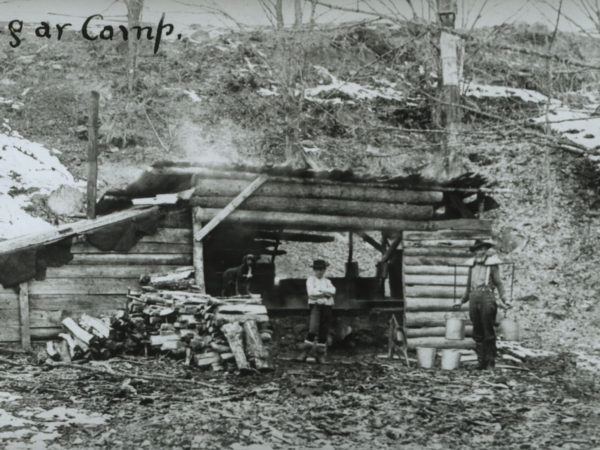 Man holding sap buckets with a yoke at sugar camp in North Creek