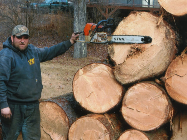 Holding up a chainsaw to a stack of logs in Elizabethtown