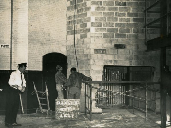 Two men work on wall supervised by guard in Glens Falls