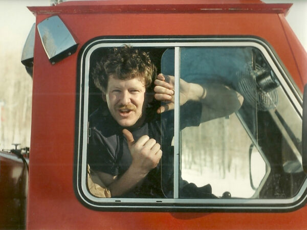 Man pokes his head out the window a red snow groomer